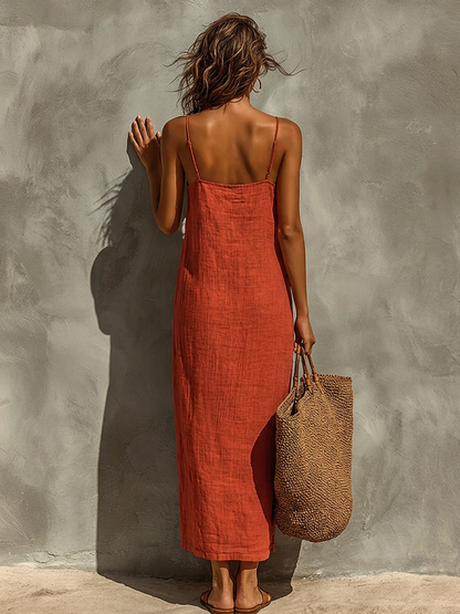 White - Woman wearing a textured maxi slip sundress with spaghetti straps, holding a large woven tote bag against a textured grey wall.