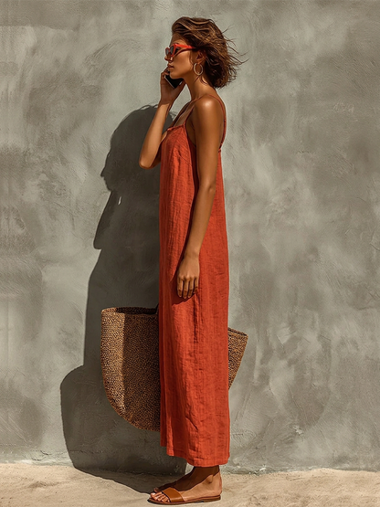 White - Woman wearing a textured maxi slip sundress with spaghetti straps, holding a large woven tote bag against a textured grey wall.