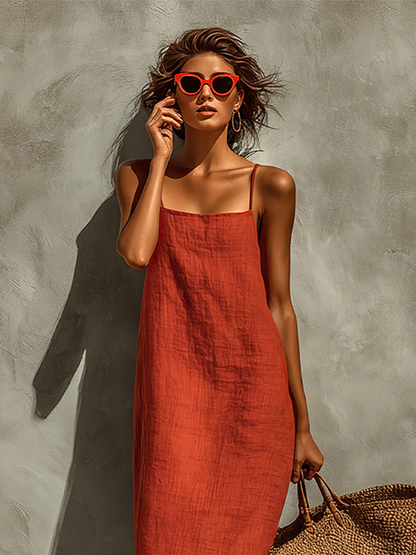 Red - Woman wearing a textured maxi slip sundress with spaghetti straps, holding a large woven tote bag against a textured grey wall.