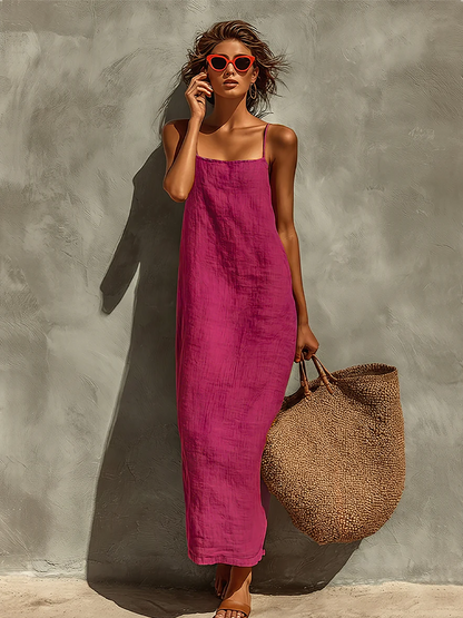 Purple - Woman wearing a textured maxi slip sundress with spaghetti straps, holding a large woven tote bag against a textured grey wall.