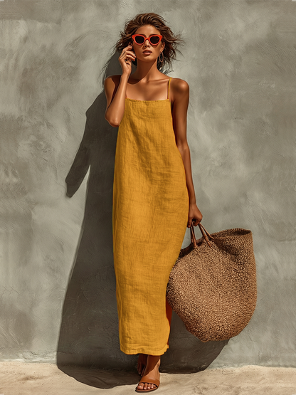 Yellow - Woman wearing a textured maxi slip sundress with spaghetti straps, holding a large woven tote bag against a textured grey wall.