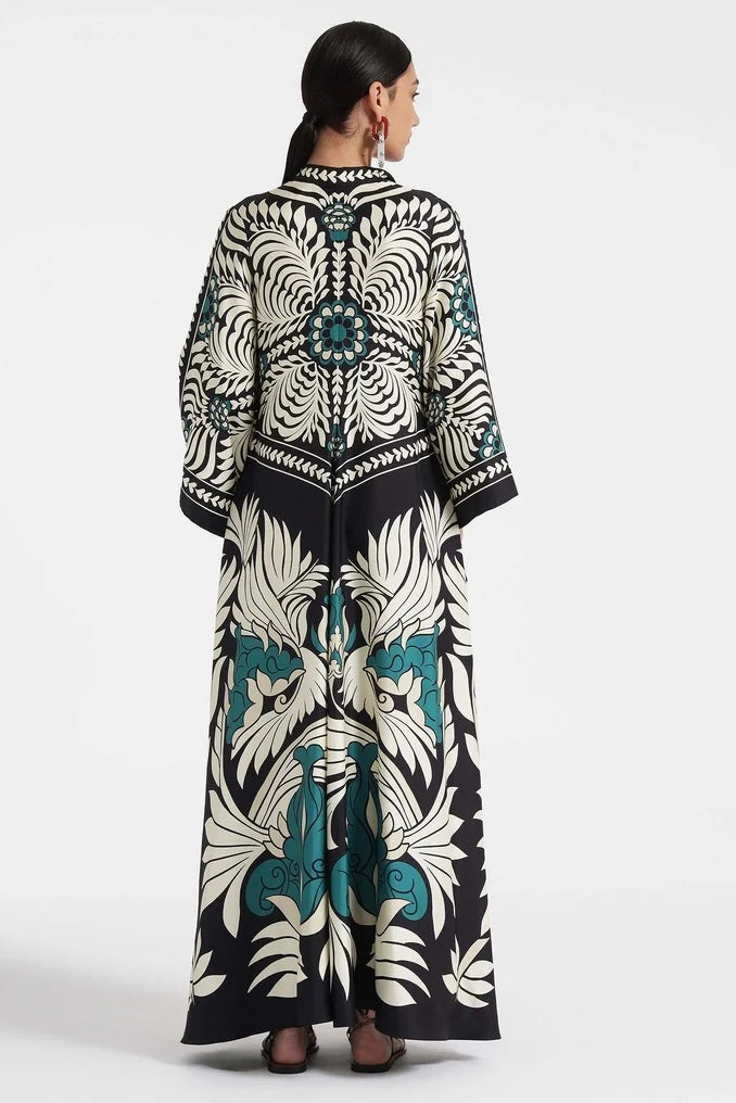 Multi - A woman wearing a high-neck maxi dress featuring a bold black, cream, and teal botanical medallion print, designed with dramatic cape sleeves and a fluid, floor-length skirt.
