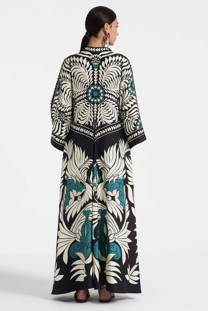 Multi - A woman wearing a high-neck maxi dress featuring a bold black, cream, and teal botanical medallion print, designed with dramatic cape sleeves and a fluid, floor-length skirt.