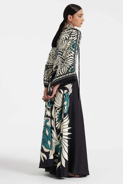 Multi - A woman wearing a high-neck maxi dress featuring a bold black, cream, and teal botanical medallion print, designed with dramatic cape sleeves and a fluid, floor-length skirt.
