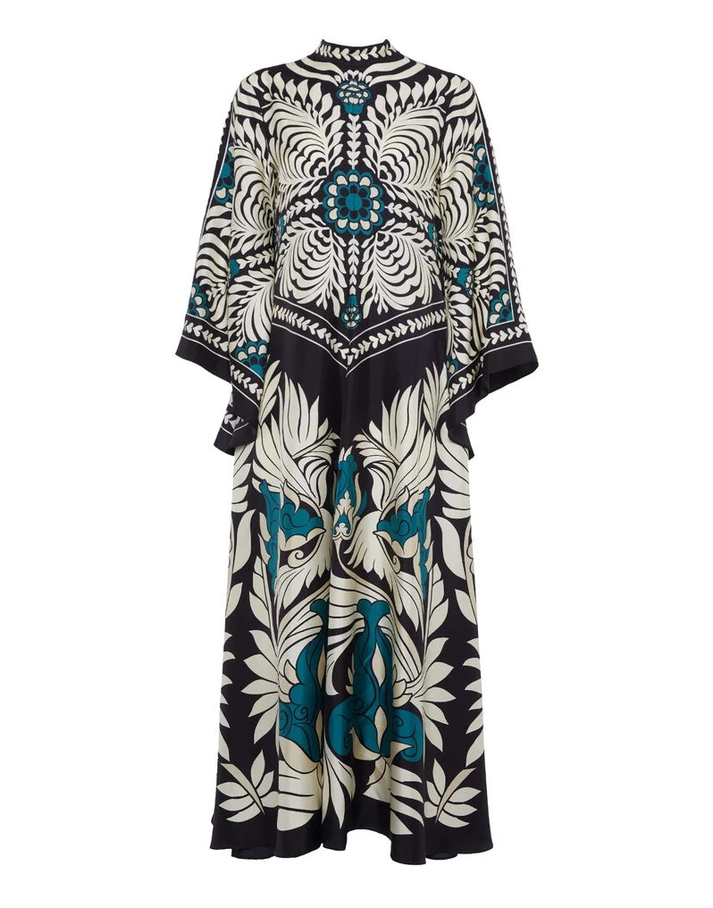 Multi - A woman wearing a high-neck maxi dress featuring a bold black, cream, and teal botanical medallion print, designed with dramatic cape sleeves and a fluid, floor-length skirt.