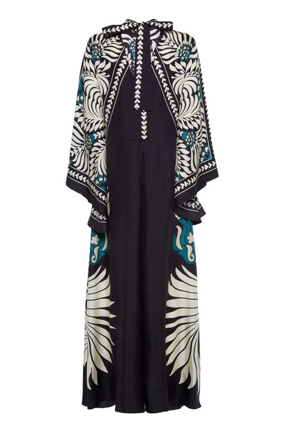 Multi - A woman wearing a high-neck maxi dress featuring a bold black, cream, and teal botanical medallion print, designed with dramatic cape sleeves and a fluid, floor-length skirt.