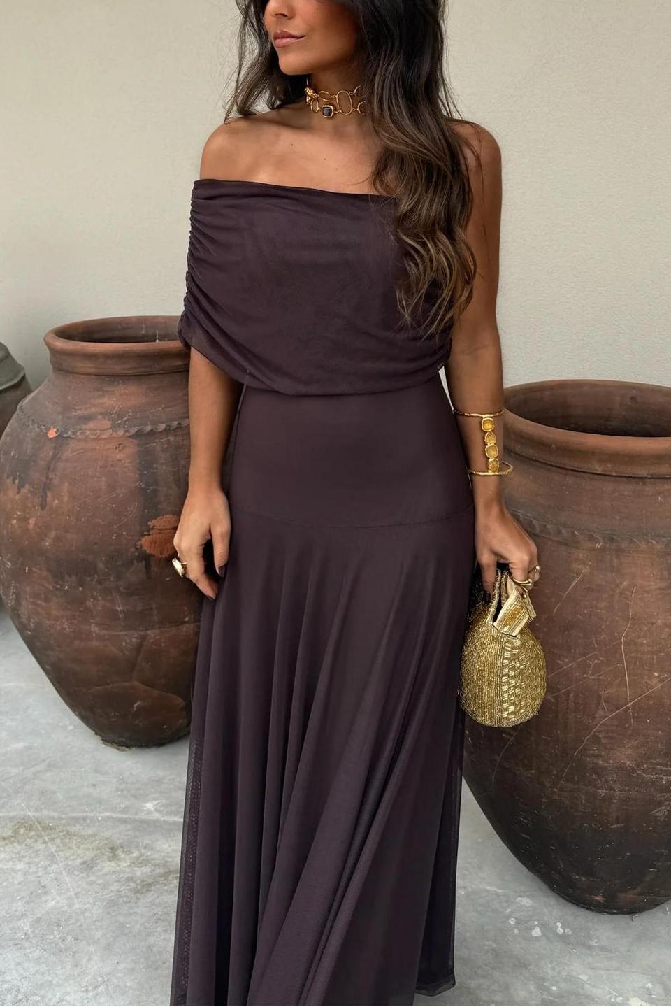 Brown - A woman wearing an elegant off-the-shoulder floor-length maxi dress featuring a ruched bodice and a sheer mesh overlay, styled with gold accessories.