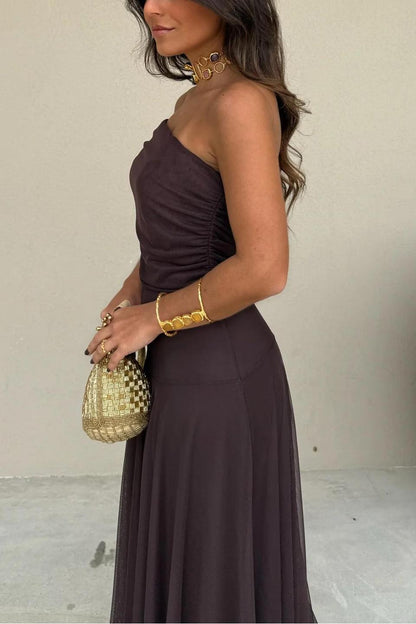 Brown - A woman wearing an elegant off-the-shoulder floor-length maxi dress featuring a ruched bodice and a sheer mesh overlay, styled with gold accessories.