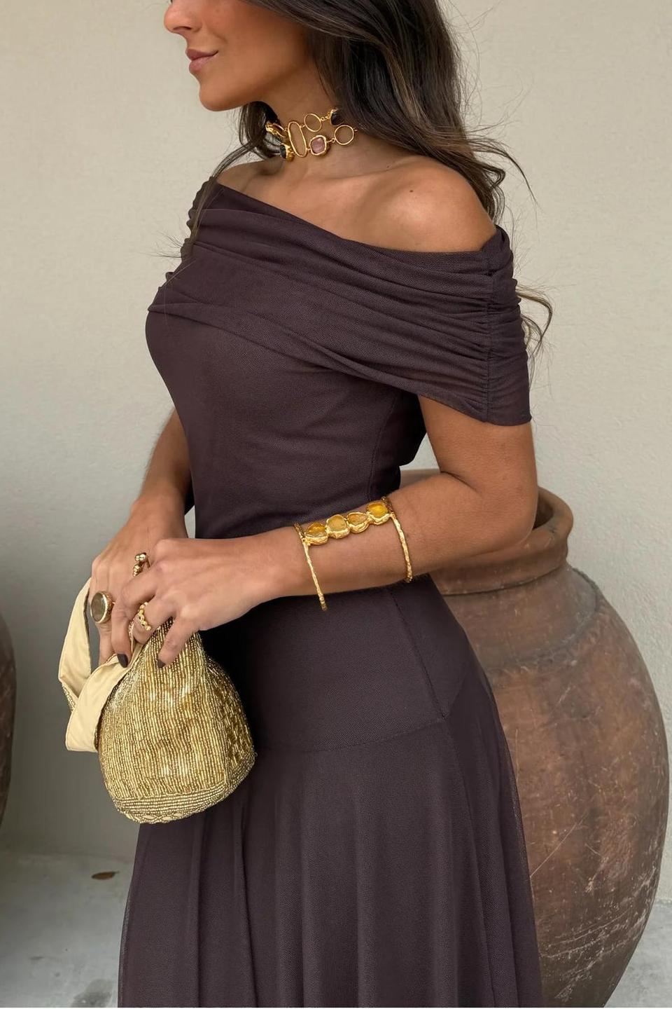 Brown - A woman wearing an elegant off-the-shoulder floor-length maxi dress featuring a ruched bodice and a sheer mesh overlay, styled with gold accessories.