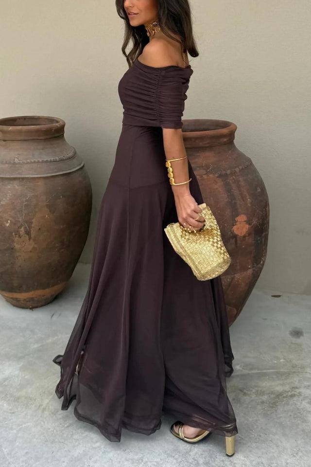 Brown - A woman wearing an elegant off-the-shoulder floor-length maxi dress featuring a ruched bodice and a sheer mesh overlay, styled with gold accessories.