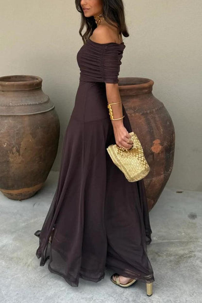 Brown - A woman wearing an elegant off-the-shoulder floor-length maxi dress featuring a ruched bodice and a sheer mesh overlay, styled with gold accessories.