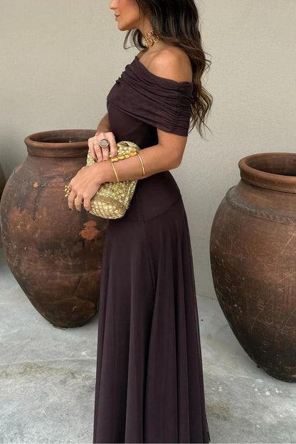 Brown - A woman wearing an elegant off-the-shoulder floor-length maxi dress featuring a ruched bodice and a sheer mesh overlay, styled with gold accessories.