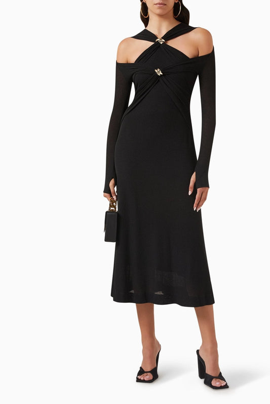 Woman in black ribbed knit midi dress with cold shoulder and gold hardware detail.