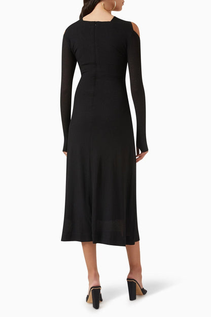 Woman in black ribbed knit midi dress with cold shoulder and gold hardware detail.