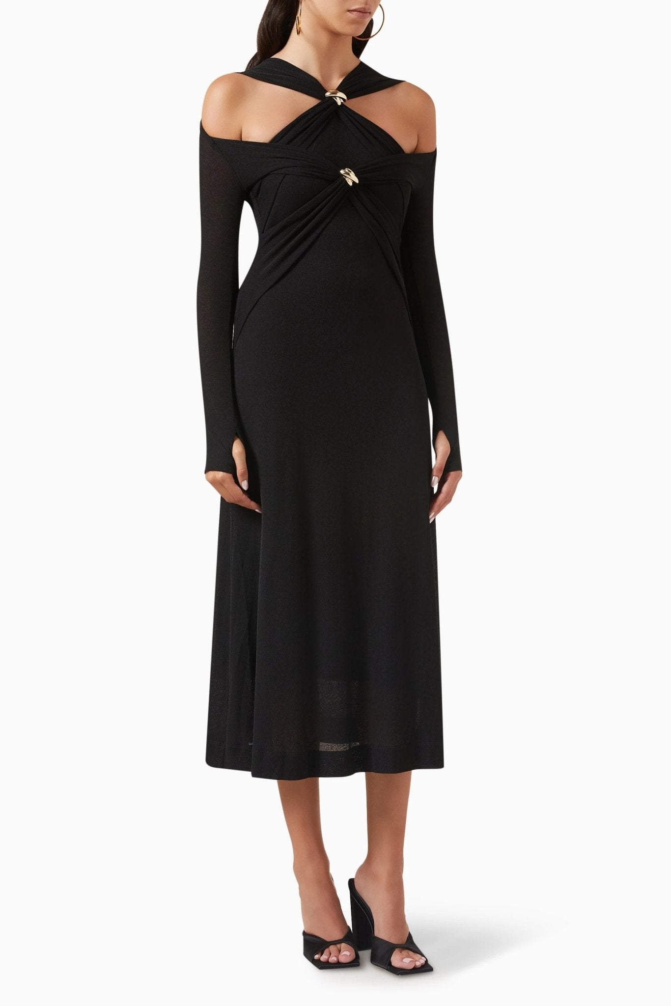 Woman in black ribbed knit midi dress with cold shoulder and gold hardware detail.