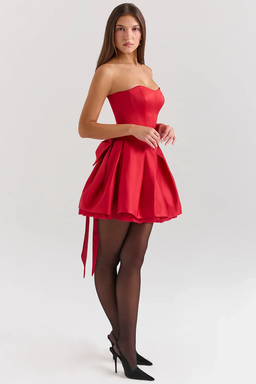 A woman models a strapless satin mini dress with a structured corset top and a full, pleated skirt.
