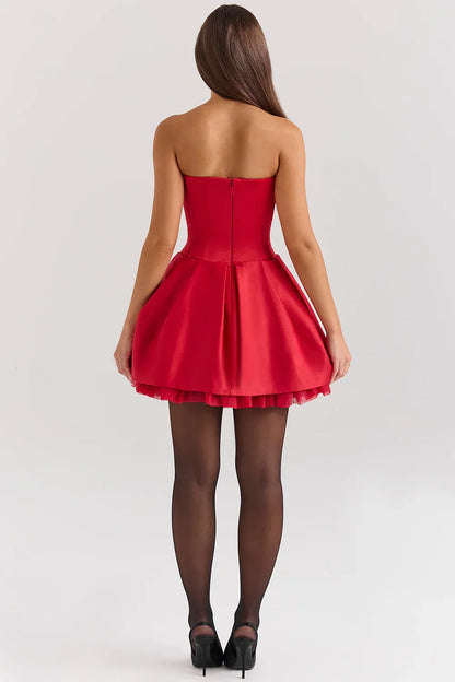 A woman models a strapless satin mini dress with a structured corset top and a full, pleated skirt.