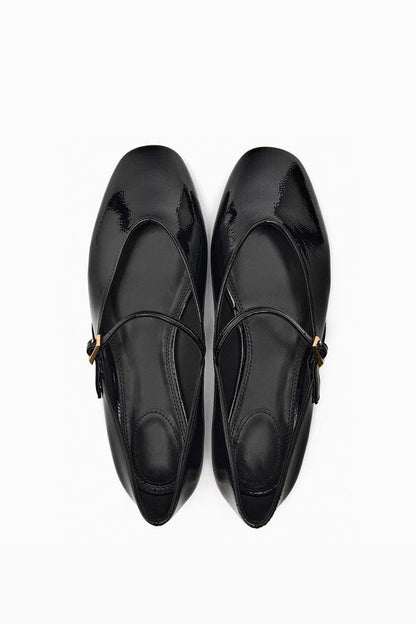 Top-down view of women's black glossy patent Mary Jane flats featuring a thin instep strap and small metallic buckle.