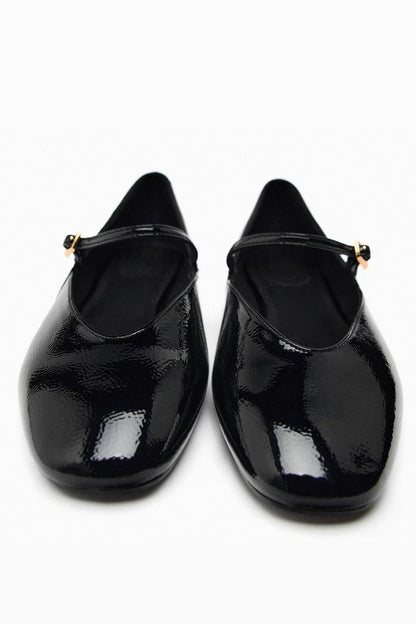 Top-down view of women's black glossy patent Mary Jane flats featuring a thin instep strap and small metallic buckle.