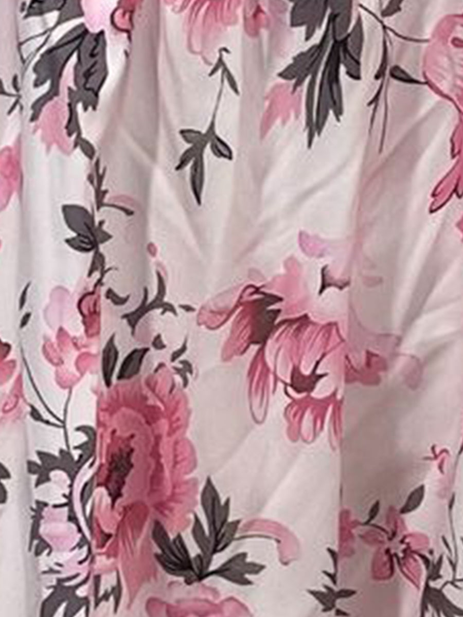 Pink - Woman wearing a floral print mini sundress with spaghetti straps, a smocked bodice, and a ruffle hem against a white textured wall