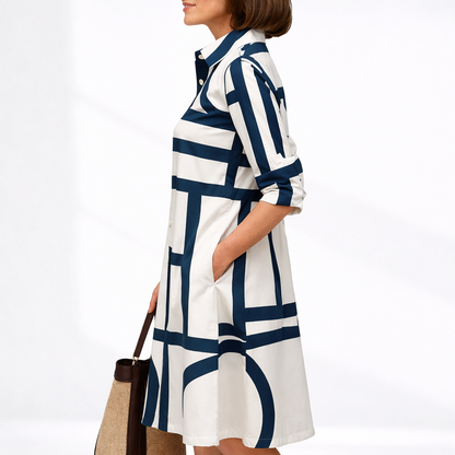 Blue & White - Woman wearing a geometric patterned button-up shirt dress with a collar and 3/4-length sleeves, holding a woven tote bag.