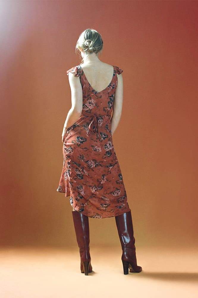 Red - A woman wearing a rust-colored, rose-printed chiffon maxi dress with ruffle cap sleeves and a scoop neckline, posing against a neutral textured backdrop.