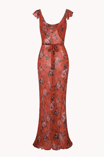 Red - A woman wearing a rust-colored, rose-printed chiffon maxi dress with ruffle cap sleeves and a scoop neckline, posing against a neutral textured backdrop.