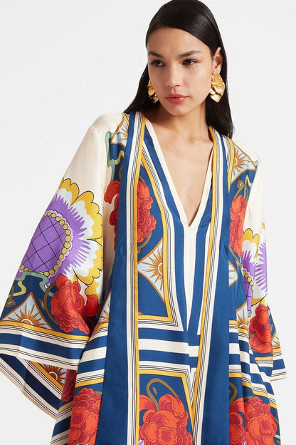 Multi - A model wears a floor-length satin maxi dress featuring a bold, colorful floral and geometric scarf print in cream, blue, red, and purple, designed with a deep V-neckline, long scarf collar, and wide flowing sleeves.