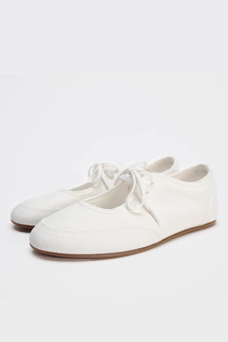 Women's white textured faux leather ballet flats with a delicate tie-front detail, viewed from above.