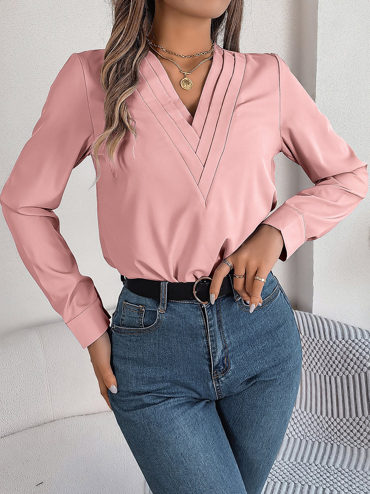 Pink - Women's long-sleeve blouse featuring a distinctive pleated V-neckline and buttoned cuffs, styled tucked into blue denim jeans.