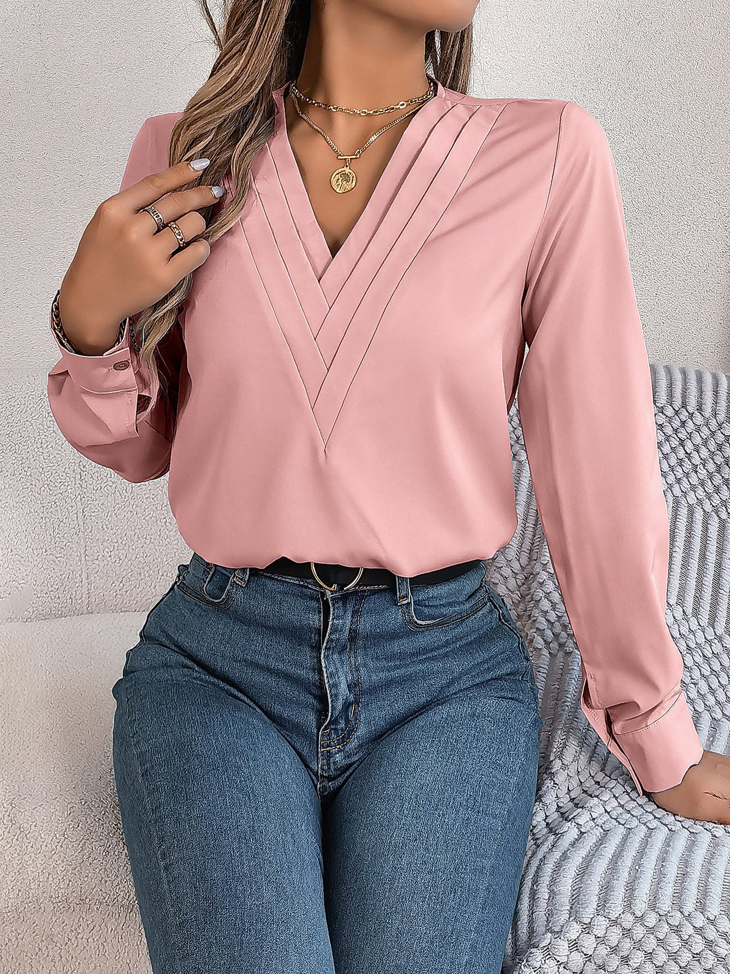 Pink - Women's long-sleeve blouse featuring a distinctive pleated V-neckline and buttoned cuffs, styled tucked into blue denim jeans.