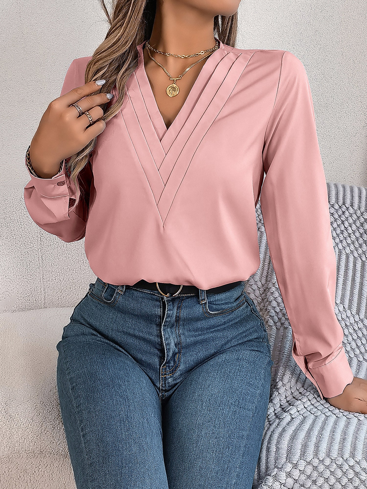 Pink - Women's long-sleeve blouse featuring a distinctive pleated V-neckline and buttoned cuffs, styled tucked into blue denim jeans.