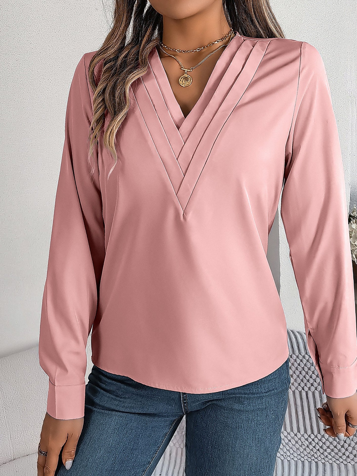 Pink - Women's long-sleeve blouse featuring a distinctive pleated V-neckline and buttoned cuffs, styled tucked into blue denim jeans.