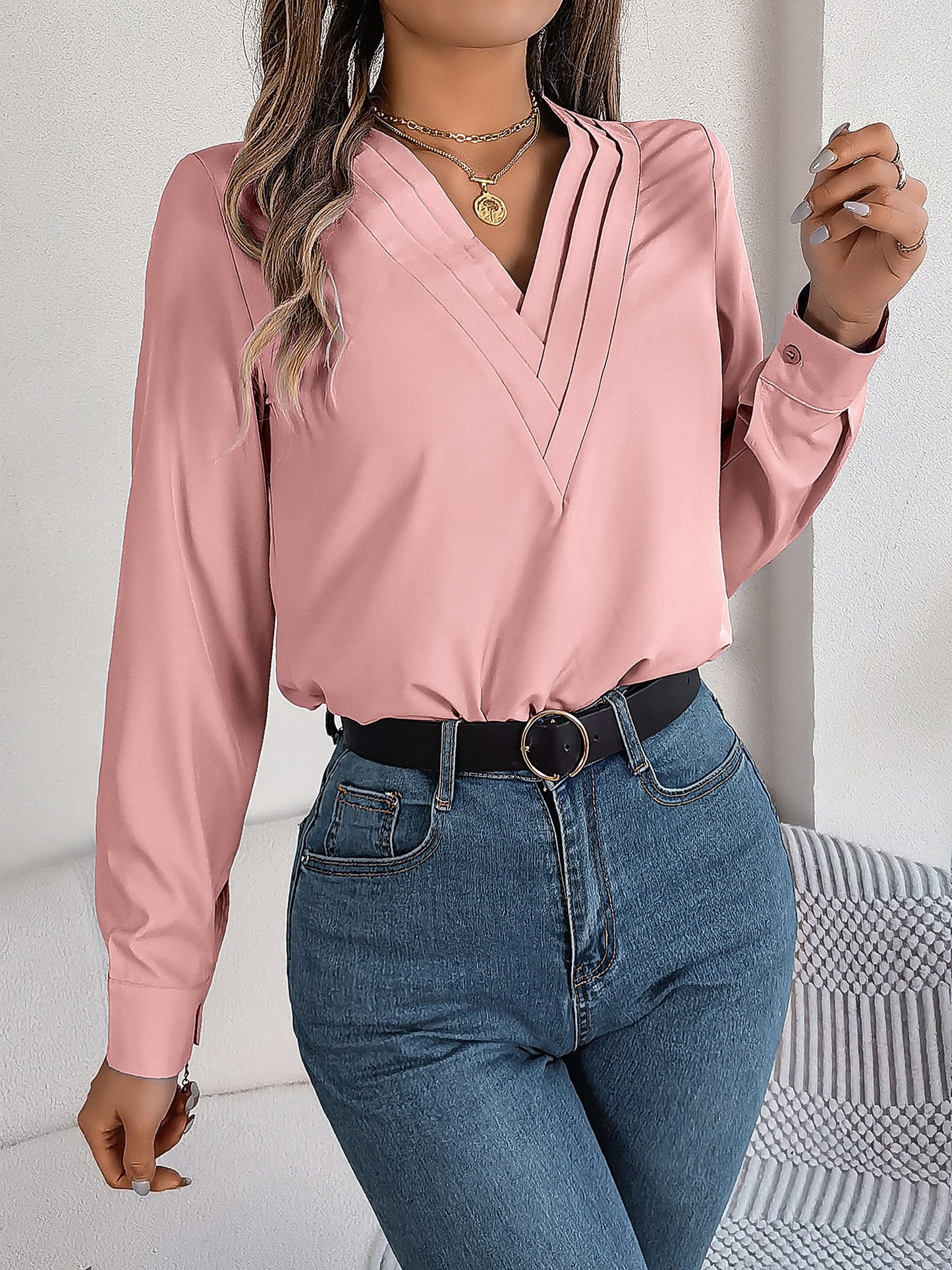 Pink - Women's long-sleeve blouse featuring a distinctive pleated V-neckline and buttoned cuffs, styled tucked into blue denim jeans.