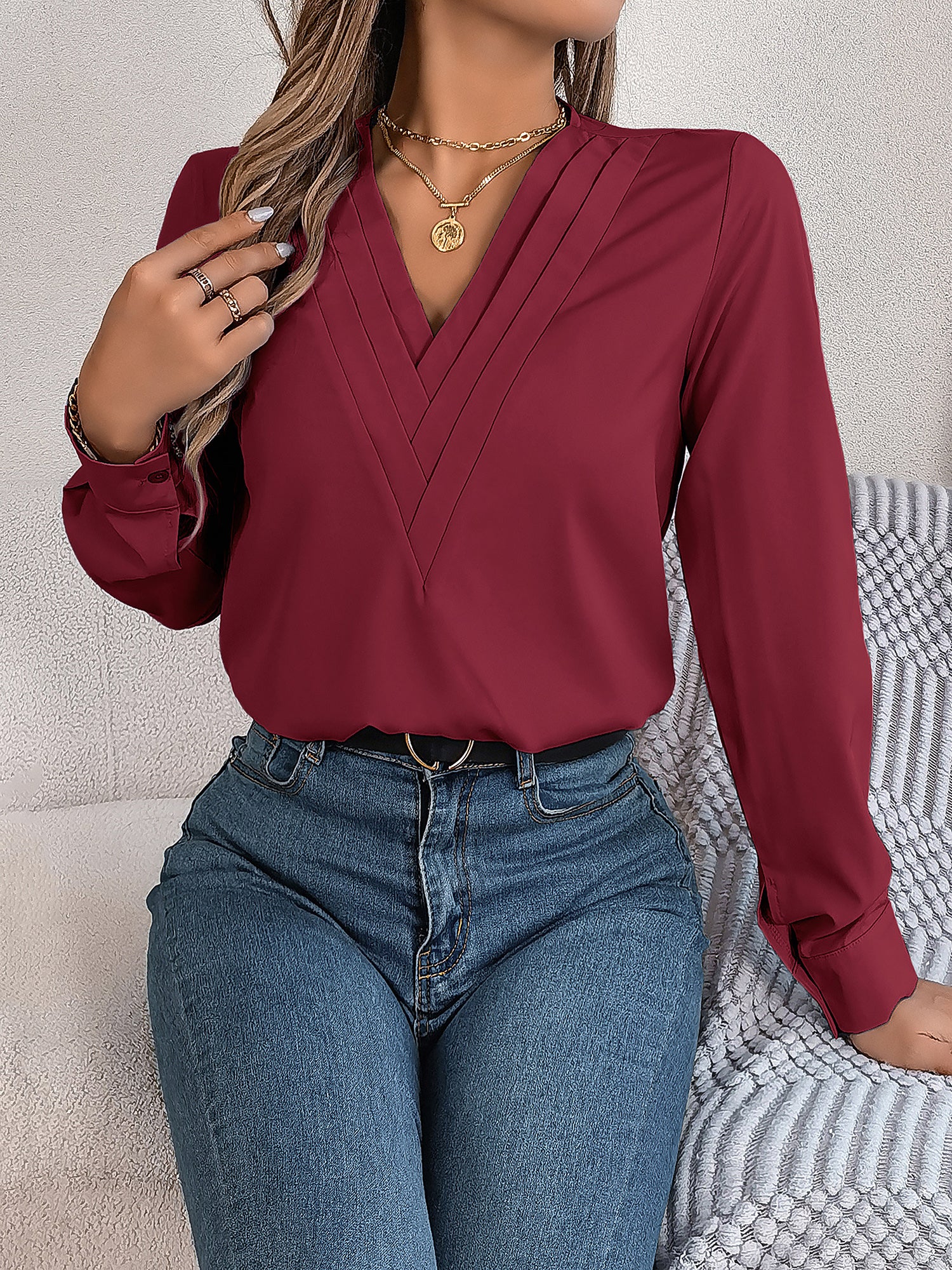 Burgundy - Women's long-sleeve blouse featuring a distinctive pleated V-neckline and buttoned cuffs, styled tucked into blue denim jeans.