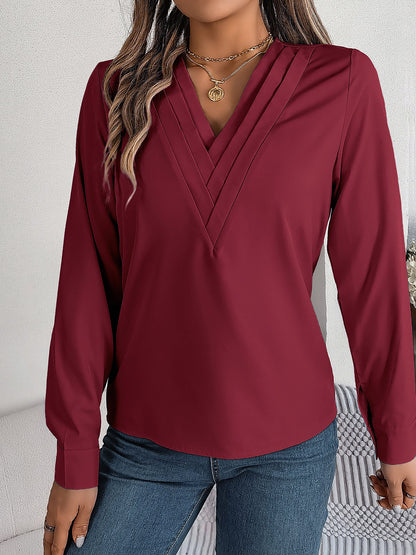 Burgundy - Women's long-sleeve blouse featuring a distinctive pleated V-neckline and buttoned cuffs, styled tucked into blue denim jeans.
