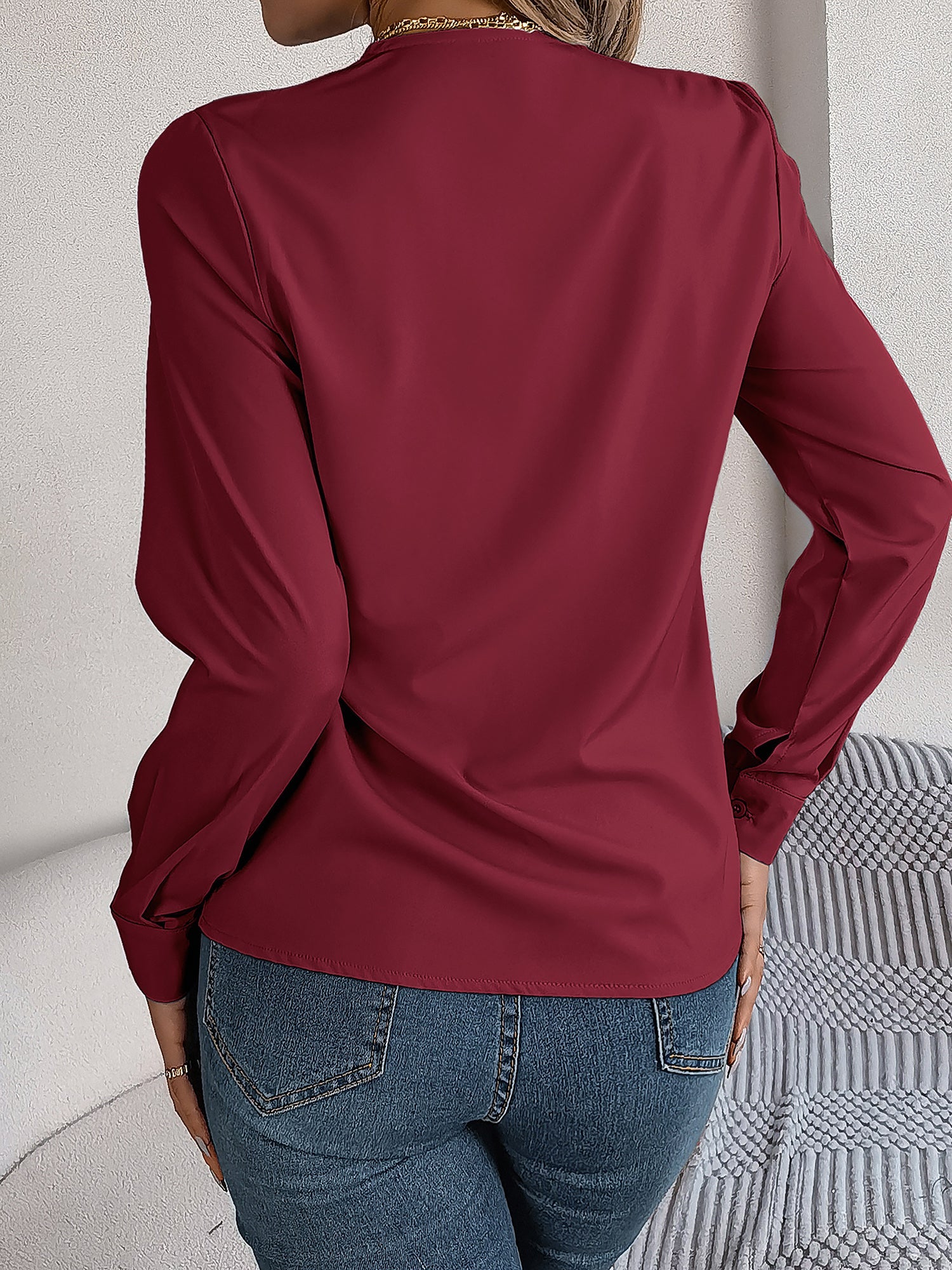 Burgundy - Women's long-sleeve blouse featuring a distinctive pleated V-neckline and buttoned cuffs, styled tucked into blue denim jeans.