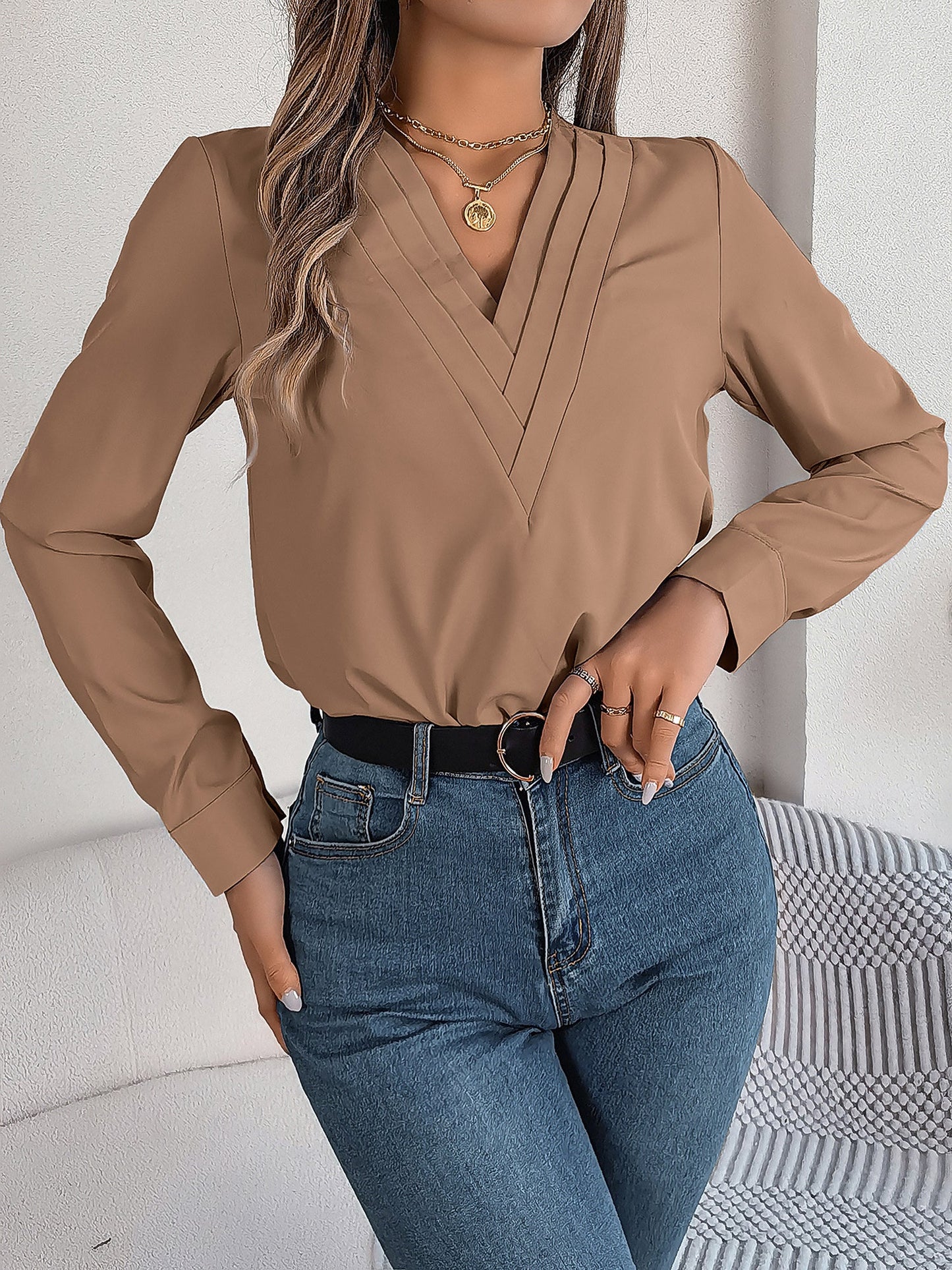 Pink - Women's long-sleeve blouse featuring a distinctive pleated V-neckline and buttoned cuffs, styled tucked into blue denim jeans.