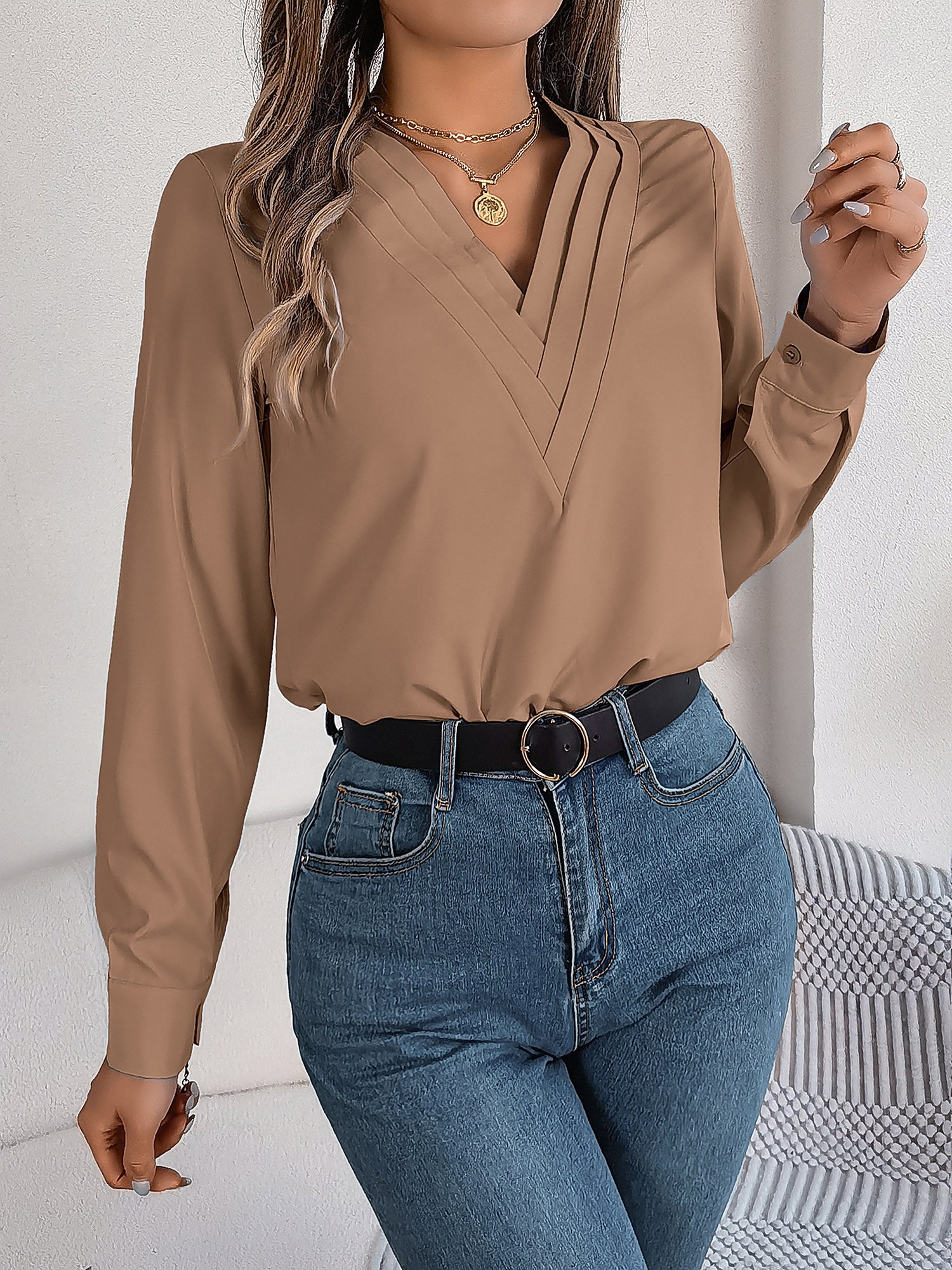 Pink - Women's long-sleeve blouse featuring a distinctive pleated V-neckline and buttoned cuffs, styled tucked into blue denim jeans.