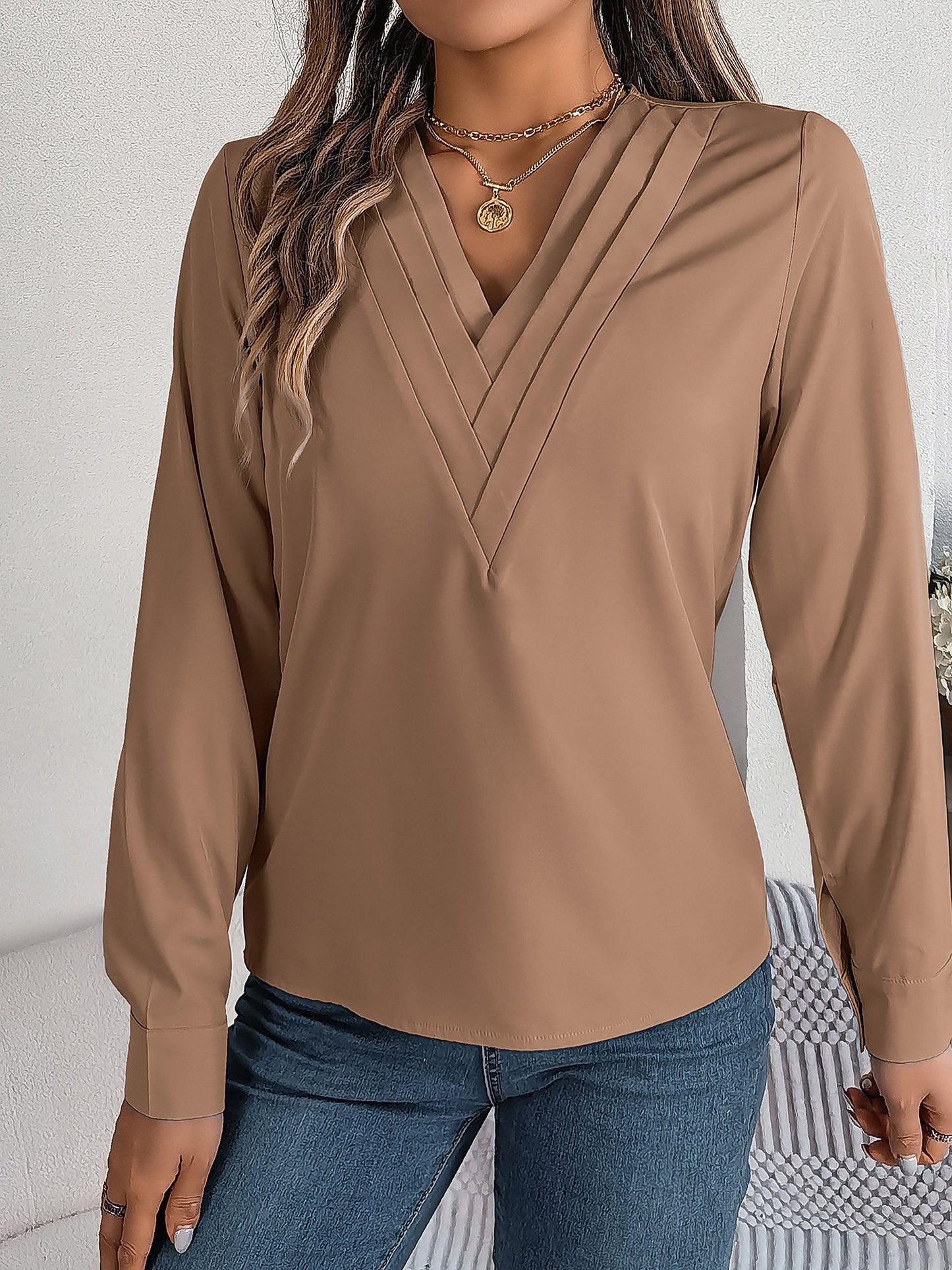 Pink - Women's long-sleeve blouse featuring a distinctive pleated V-neckline and buttoned cuffs, styled tucked into blue denim jeans.