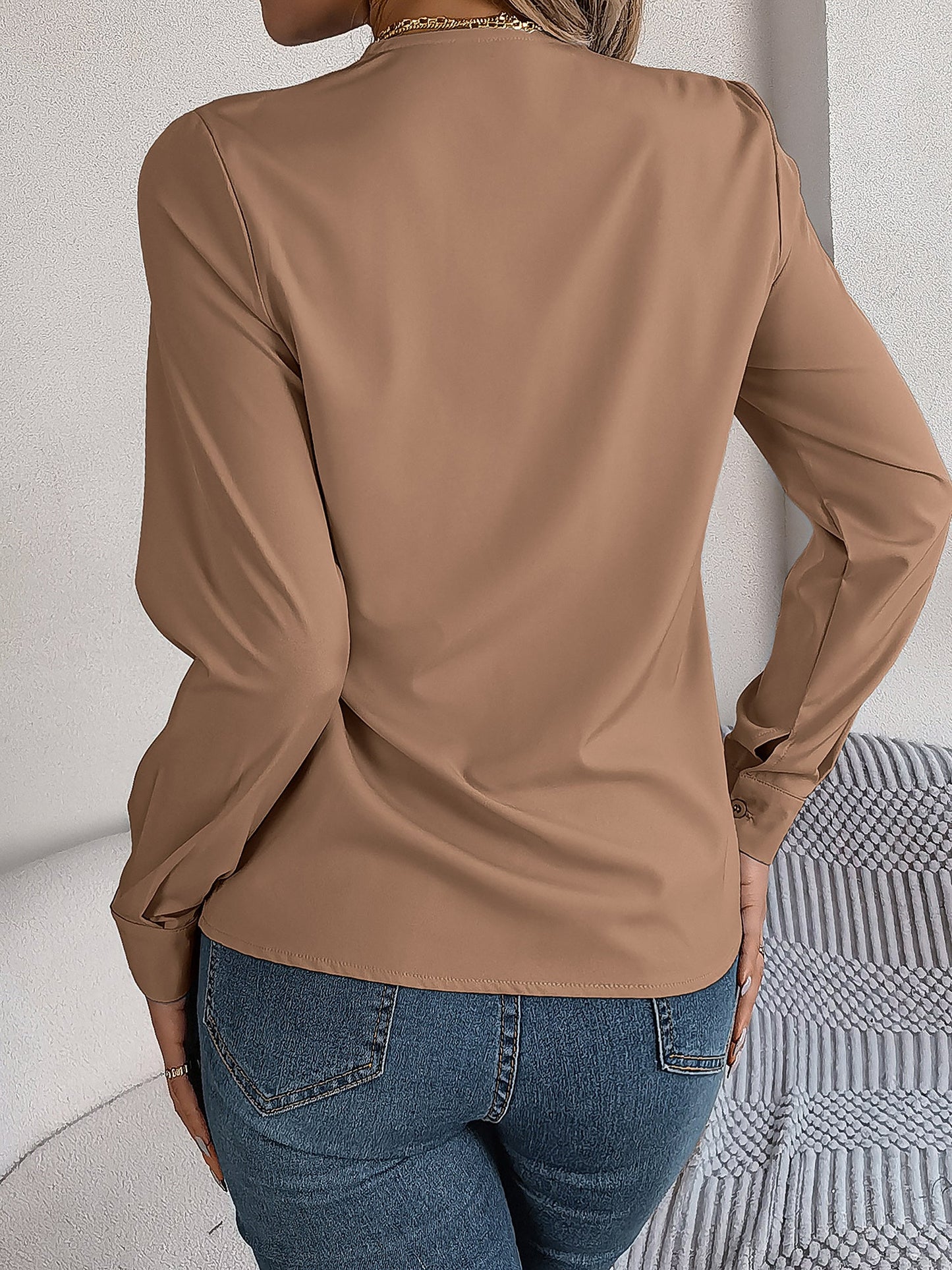 Pink - Women's long-sleeve blouse featuring a distinctive pleated V-neckline and buttoned cuffs, styled tucked into blue denim jeans.