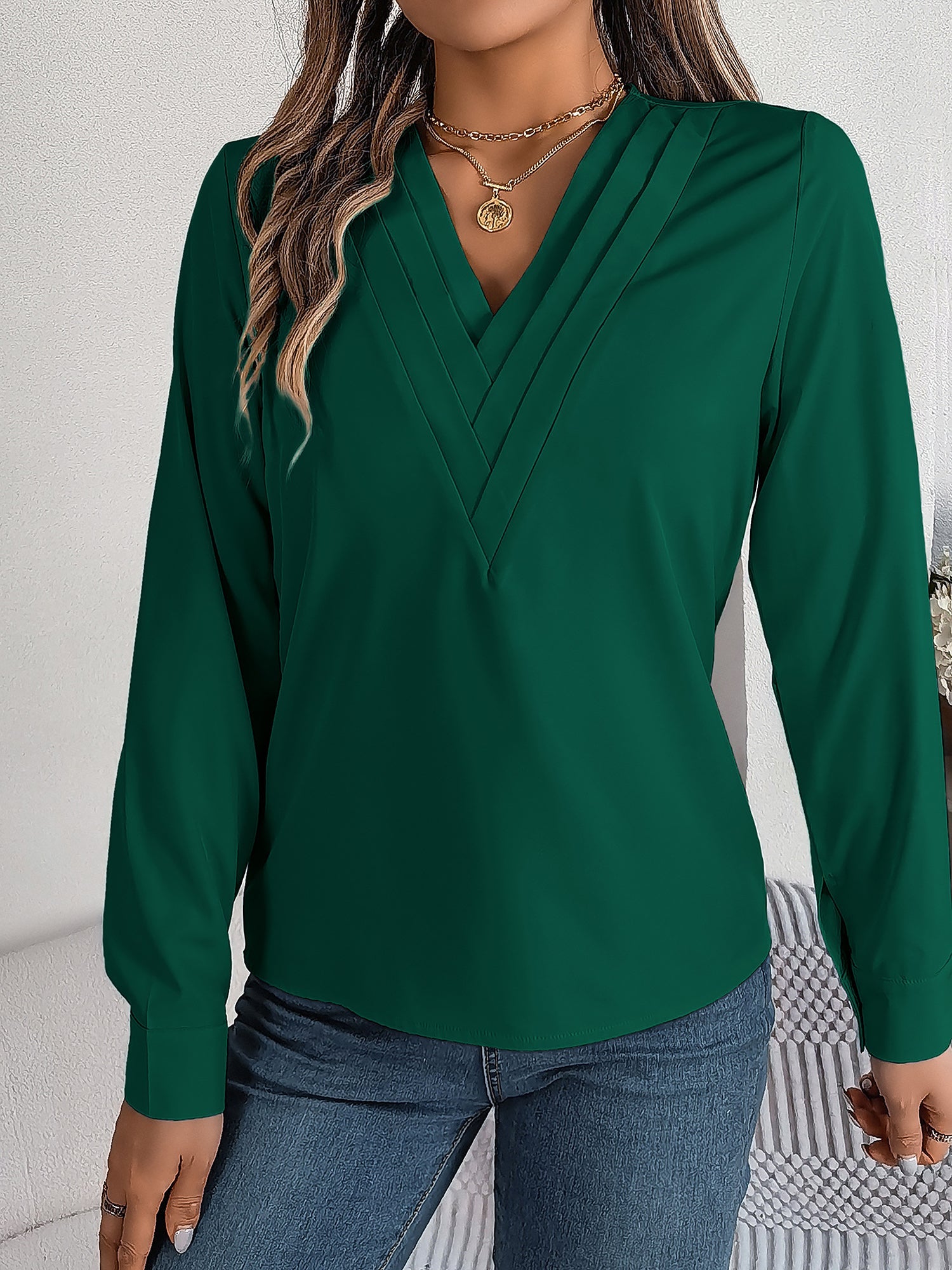 Burgundy - Women's long-sleeve blouse featuring a distinctive pleated V-neckline and buttoned cuffs, styled tucked into blue denim jeans.