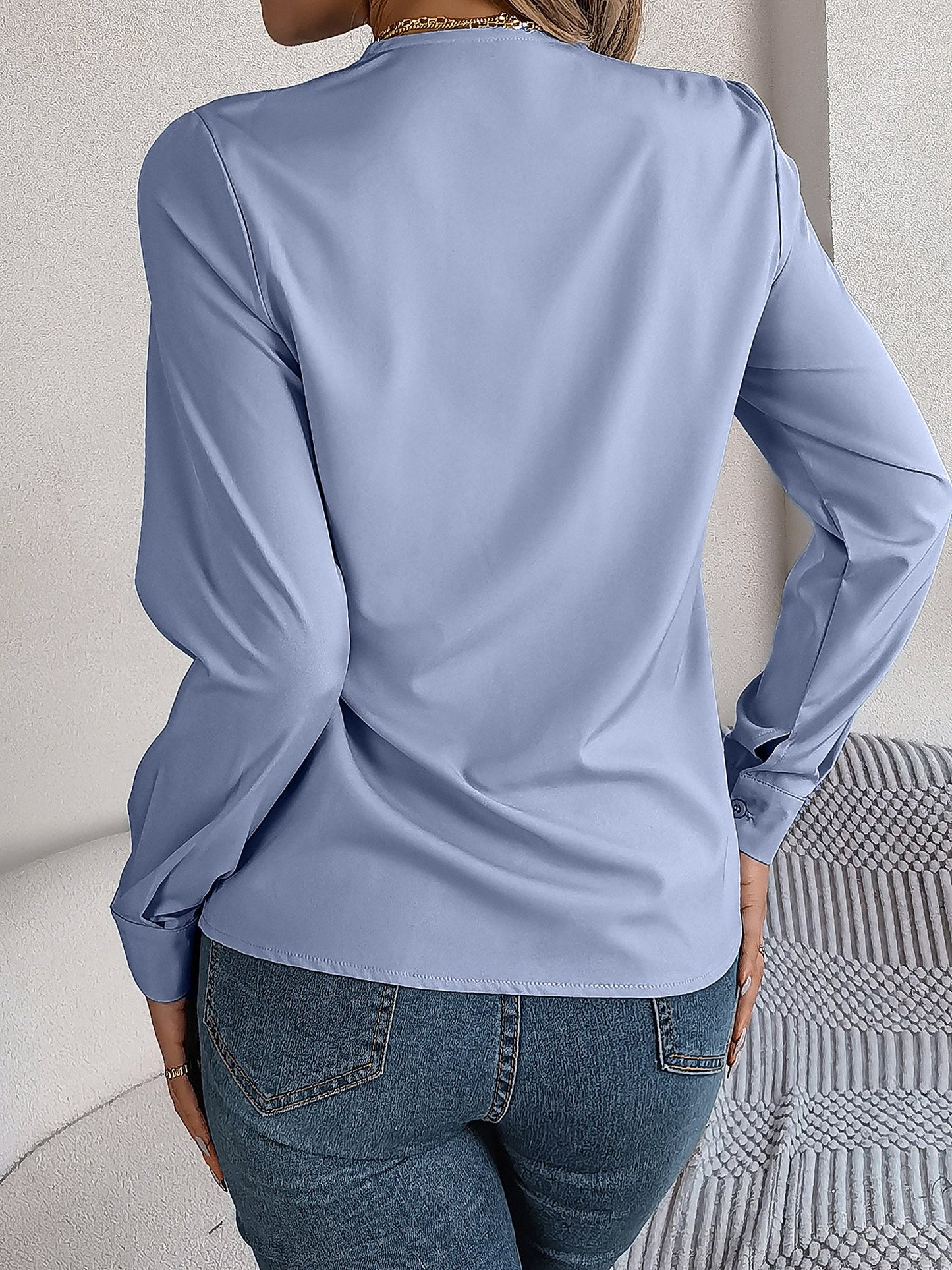 Blue - Women's long-sleeve blouse featuring a distinctive pleated V-neckline and buttoned cuffs, styled tucked into blue denim jeans.