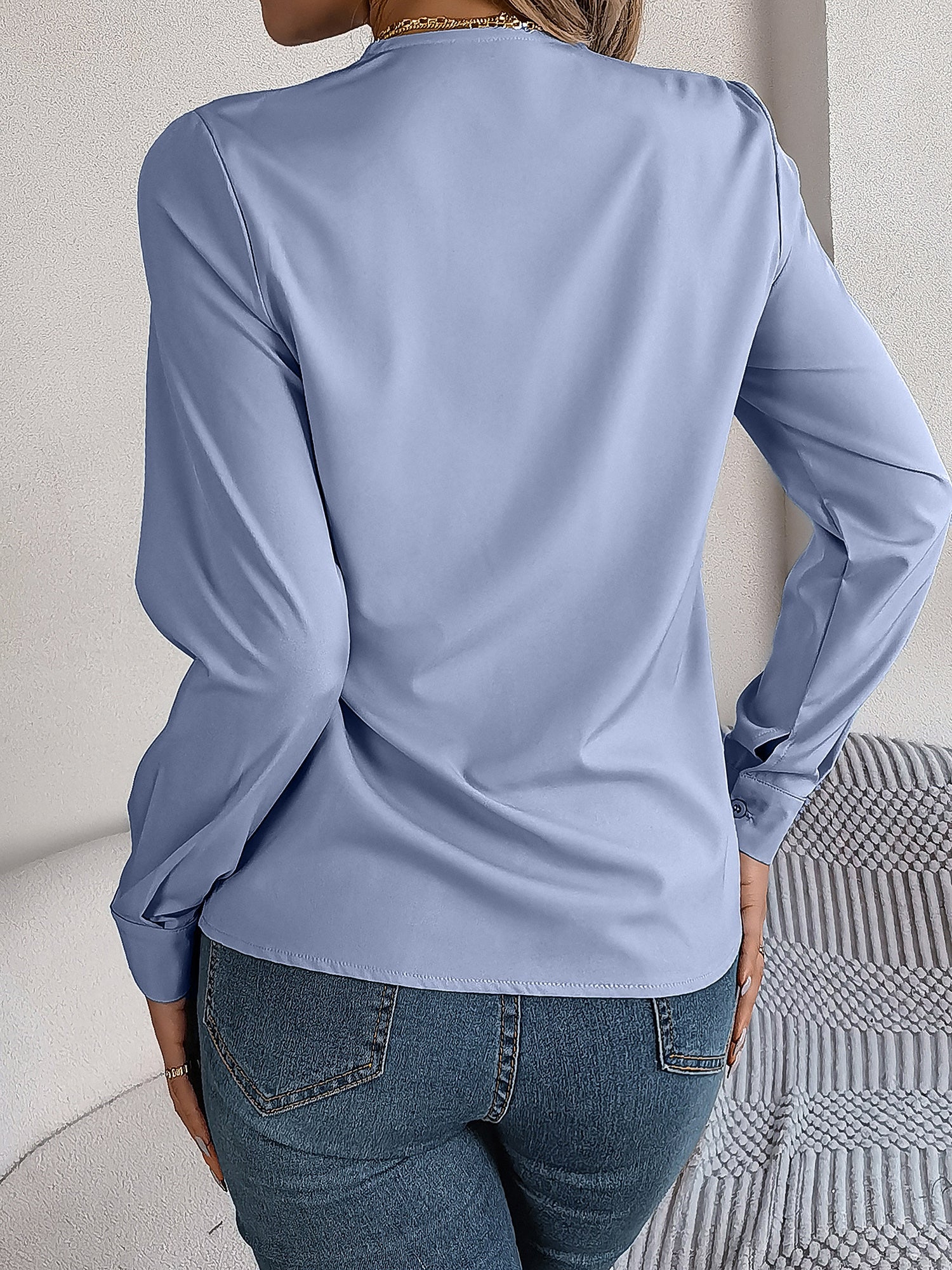Blue - Women's long-sleeve blouse featuring a distinctive pleated V-neckline and buttoned cuffs, styled tucked into blue denim jeans.