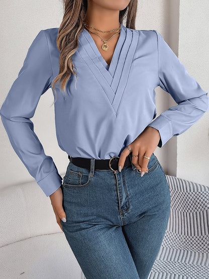 Blue - Women's long-sleeve blouse featuring a distinctive pleated V-neckline and buttoned cuffs, styled tucked into blue denim jeans.