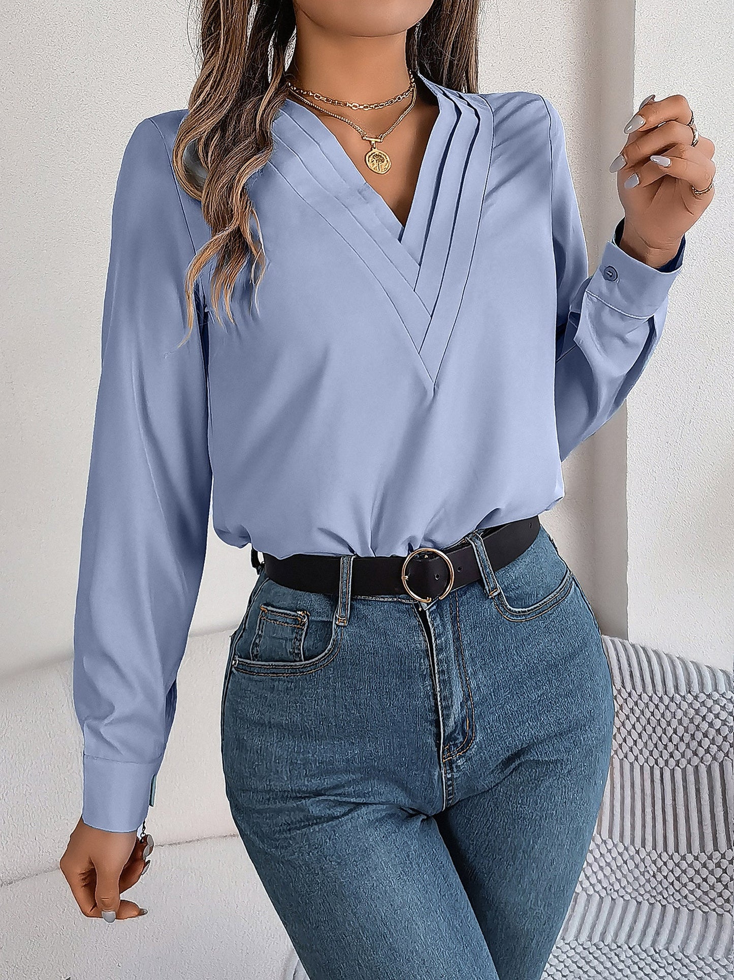 Blue - Women's long-sleeve blouse featuring a distinctive pleated V-neckline and buttoned cuffs, styled tucked into blue denim jeans.