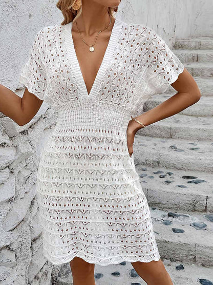 White - A woman wears a white, short-sleeve mini cover-up featuring a deep V-neck, a wide smocked waist, and an all-over geometric open-knit pattern.