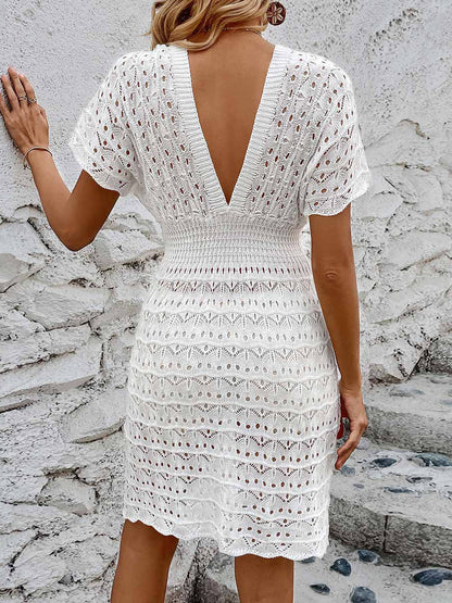 White - A woman wears a white, short-sleeve mini cover-up featuring a deep V-neck, a wide smocked waist, and an all-over geometric open-knit pattern.