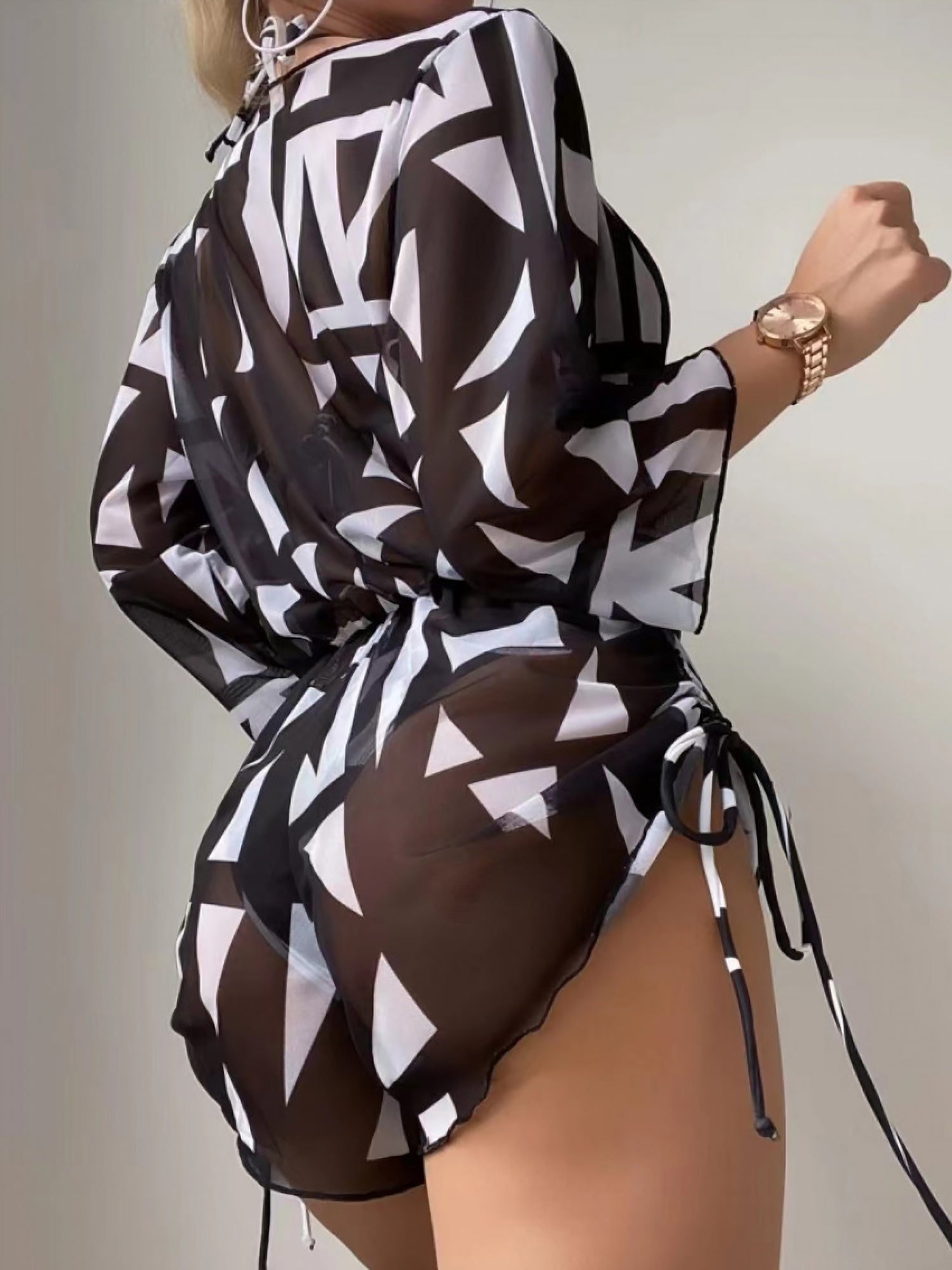 Black - A woman models a sheer, short-sleeve mini cover-up with a vibrant tropical leaf print in shades of purple, blue, and pink, featuring a deep V-neck, drawstring waist, and ruched sides with ties.