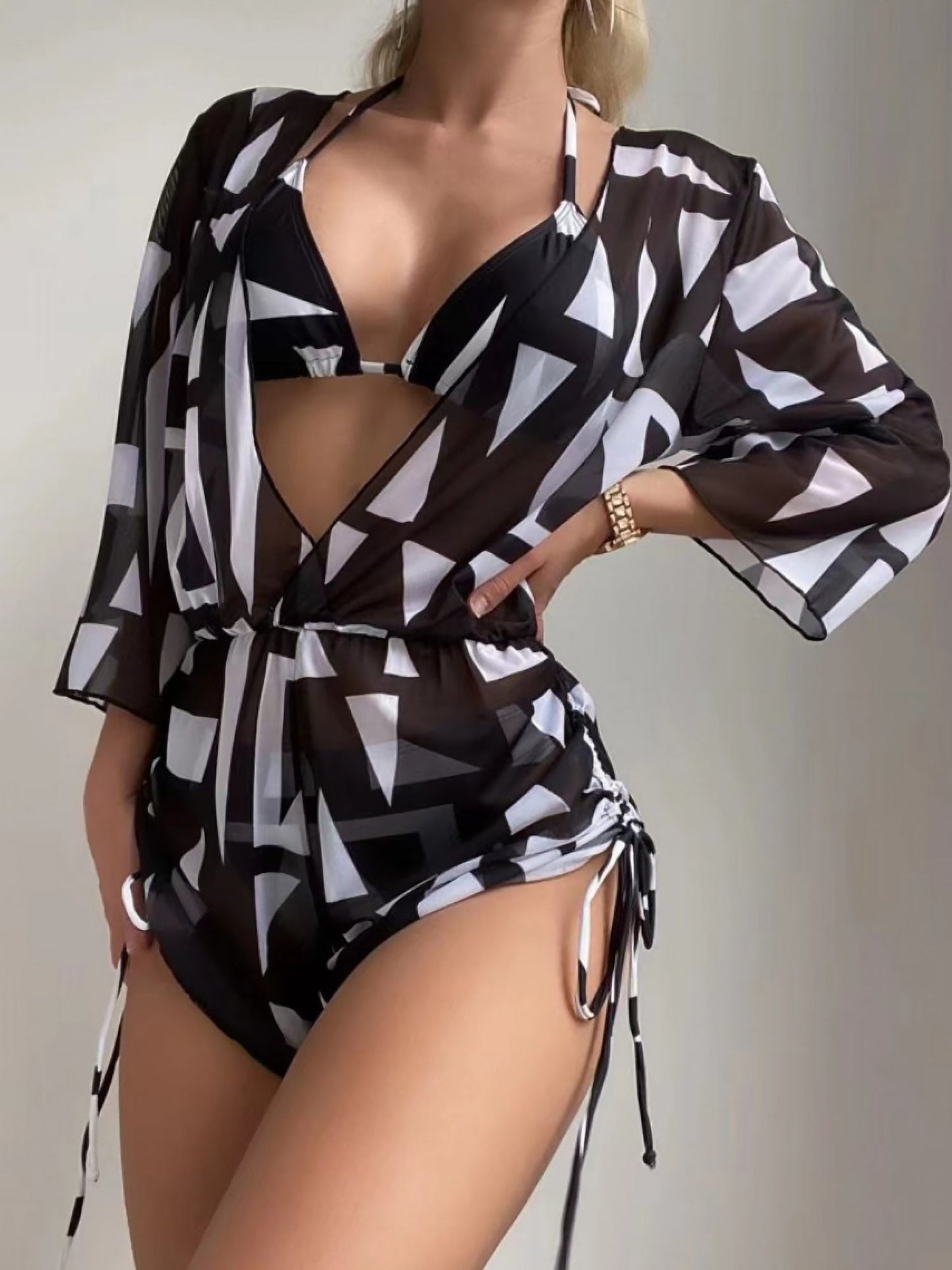 Black - A woman models a sheer, short-sleeve mini cover-up with a vibrant tropical leaf print in shades of purple, blue, and pink, featuring a deep V-neck, drawstring waist, and ruched sides with ties.